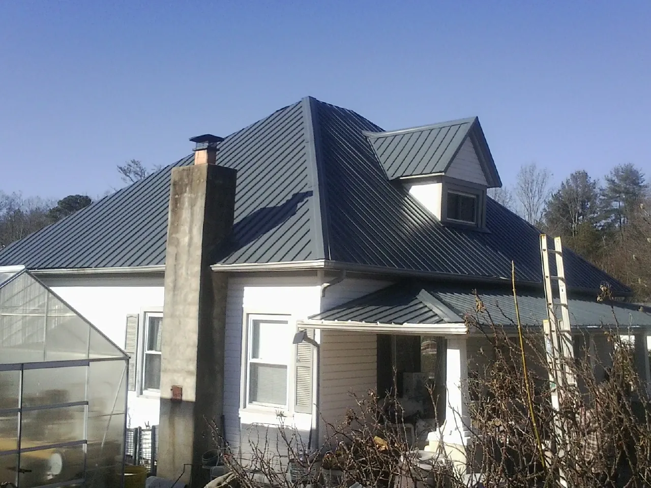 Dark blue standing seam metal roof on a white farmhouse with dormer — Slate & Tile Roof Repair by Roofing Brothers in Renfrew