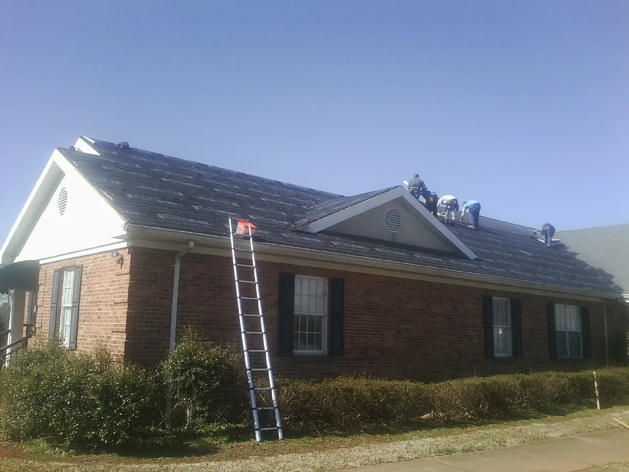 Crew tearing shingles off a brick ranch roof with a ladder set — Emergency Roof Repair work by our crew in Renfrew