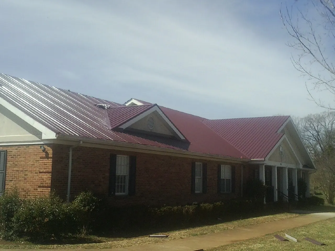 Red metal roof with gabled entries on a long brick building, from a Hail Damage Roof Repair job in Renfrew