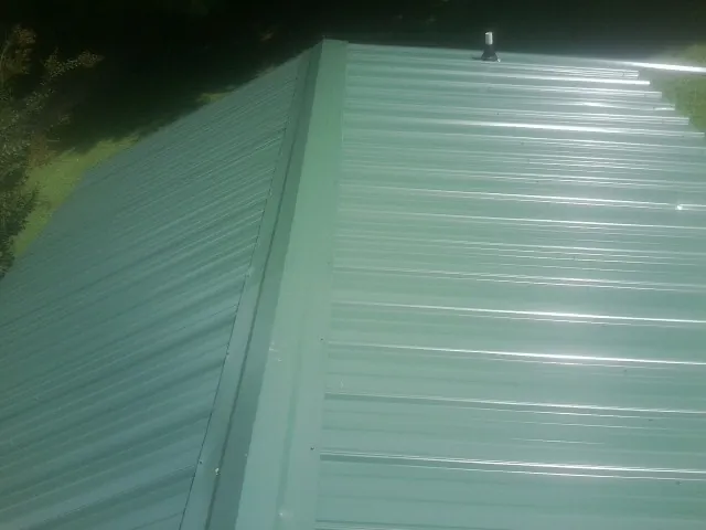 New green metal panels meeting at the ridge of a roof — Flat Roof Repair work by our crew in Renfrew