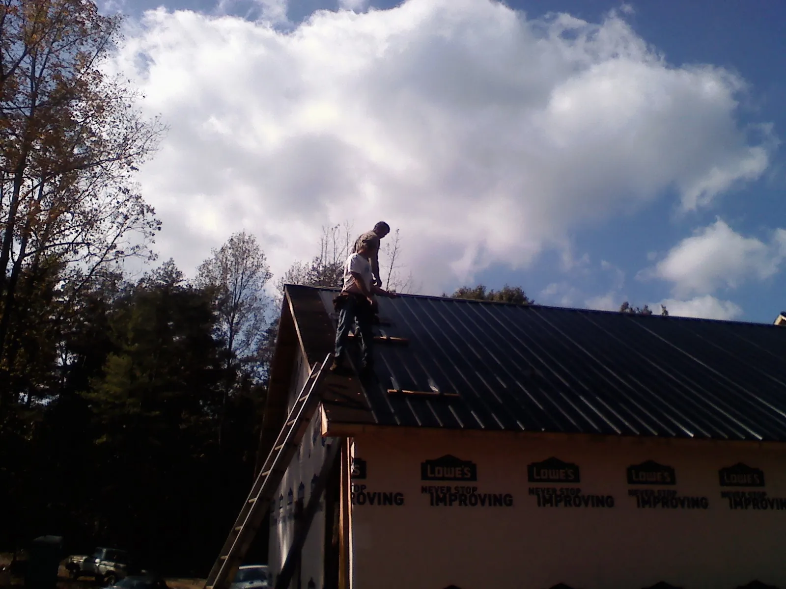 Roofer fastening dark metal panels high against a cloudy sky, from a Roof Inspection job in Renfrew