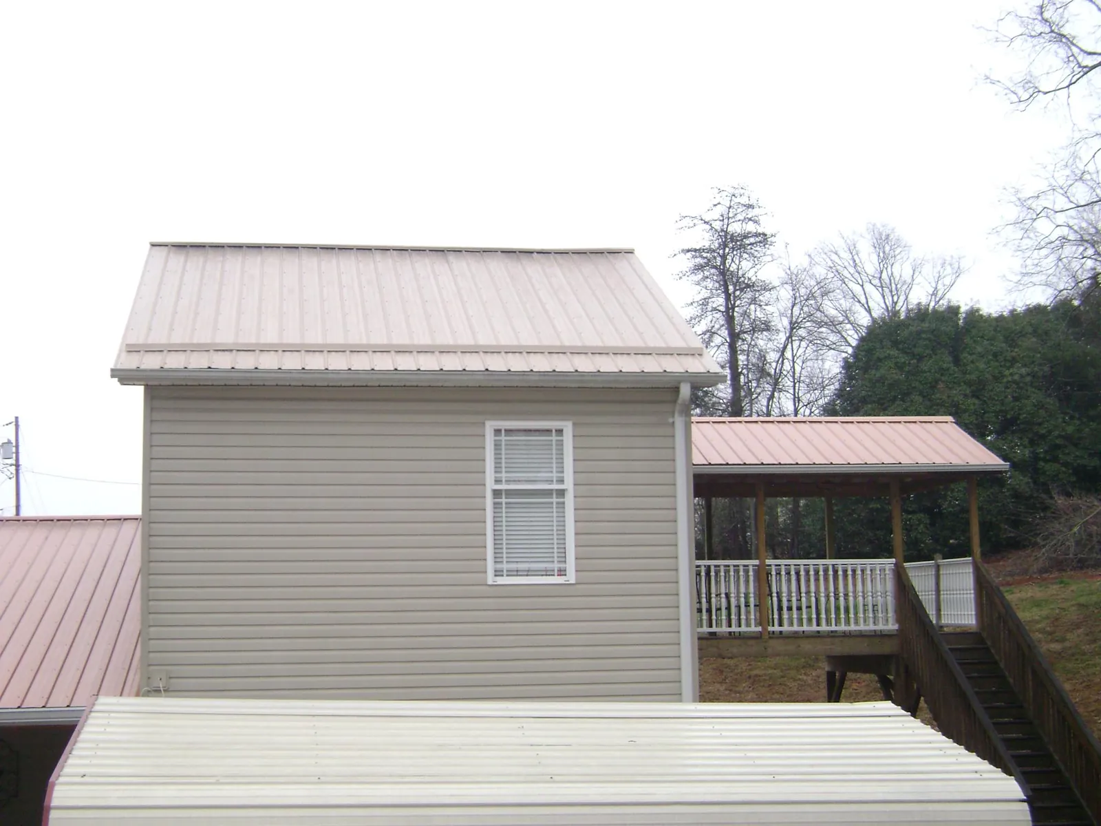 Tan metal roofs on a two story addition and attached porch, from a Roof Replacement job in Renfrew